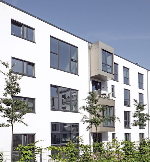 A modern white apartment house with small trees in the foreground